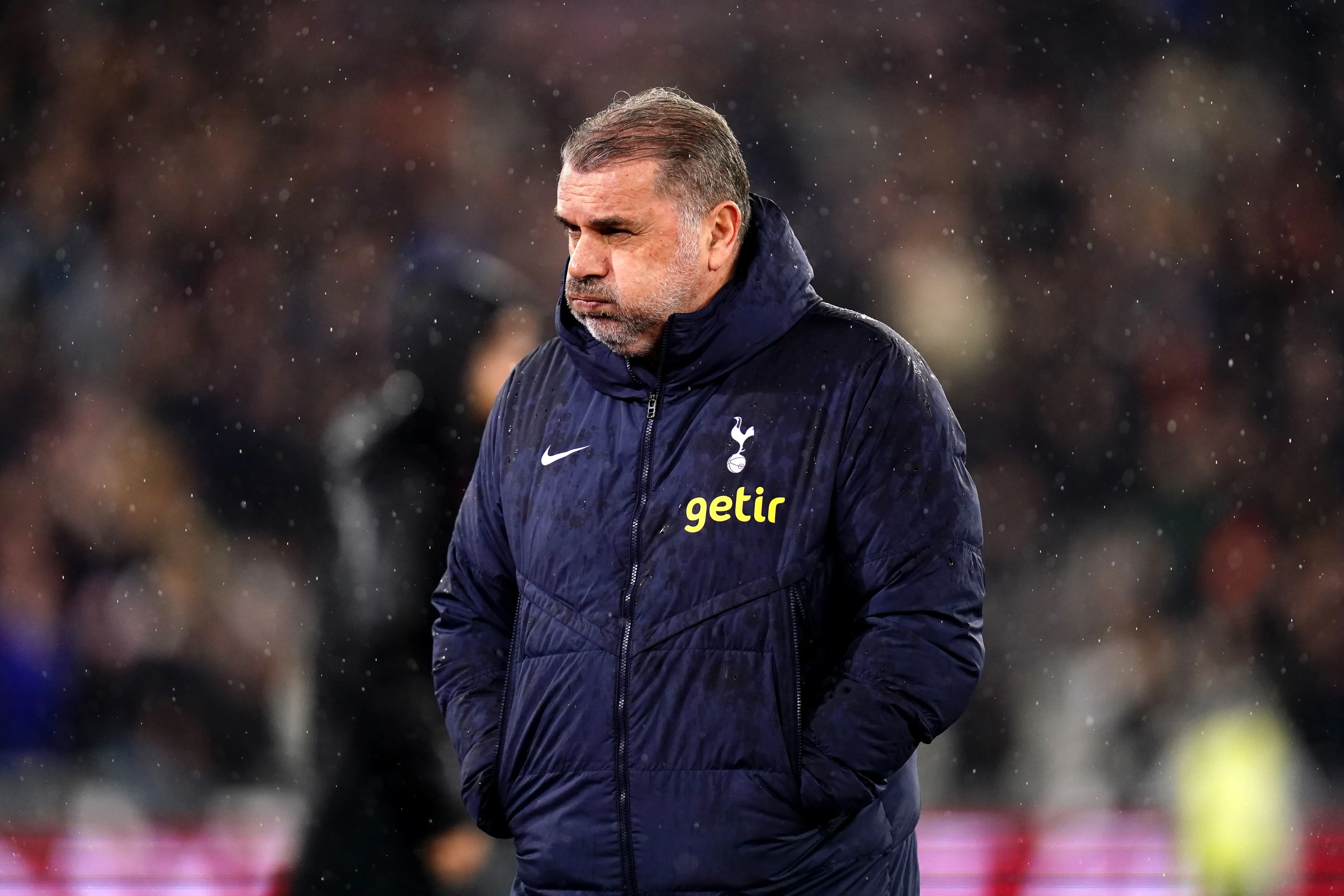 Ange Postecoglou in a Tottenham coat, looking thoughtful during a match.