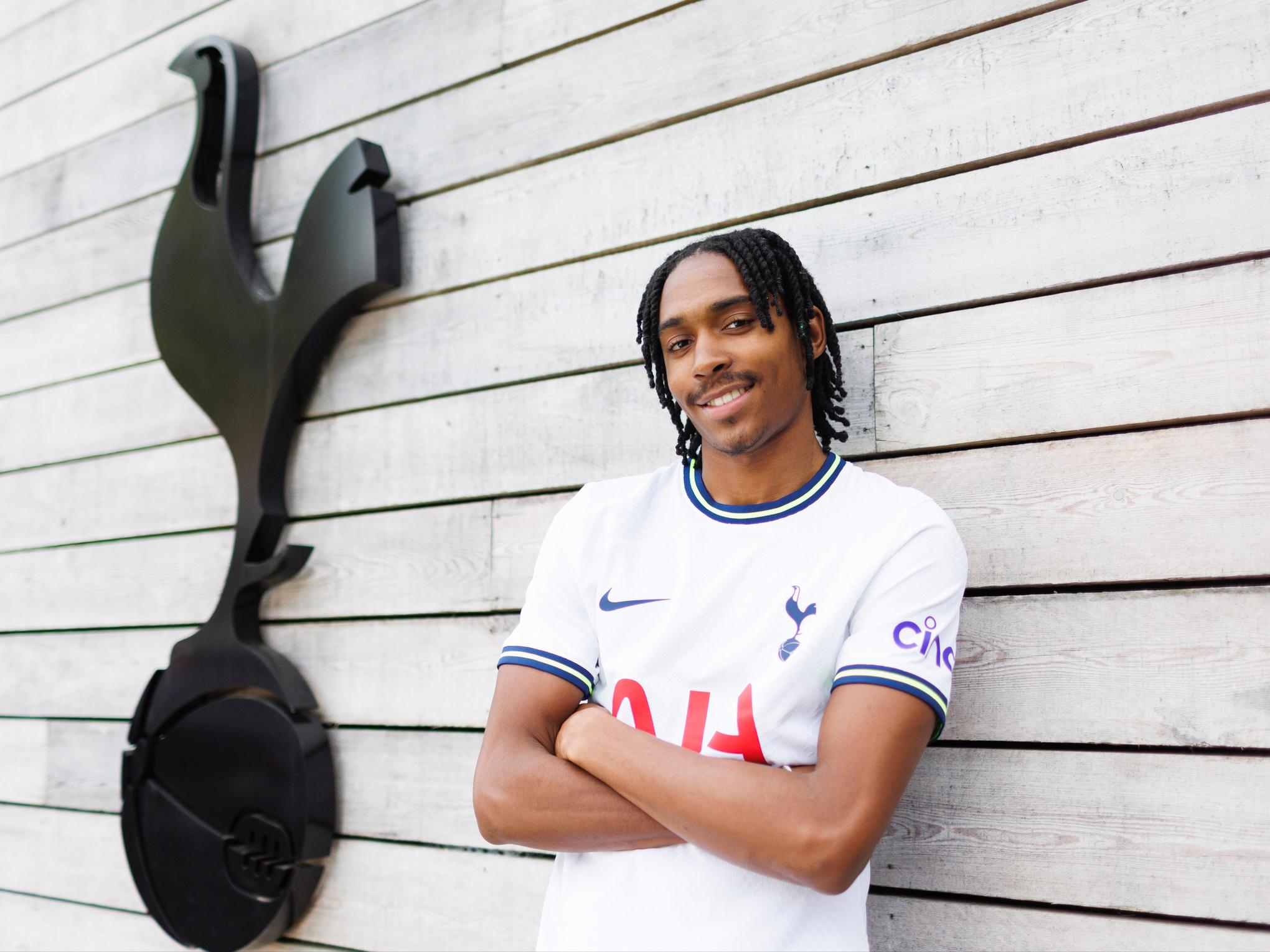 Djed Spence posing in a Tottenham Hotspur jersey near the club logo.