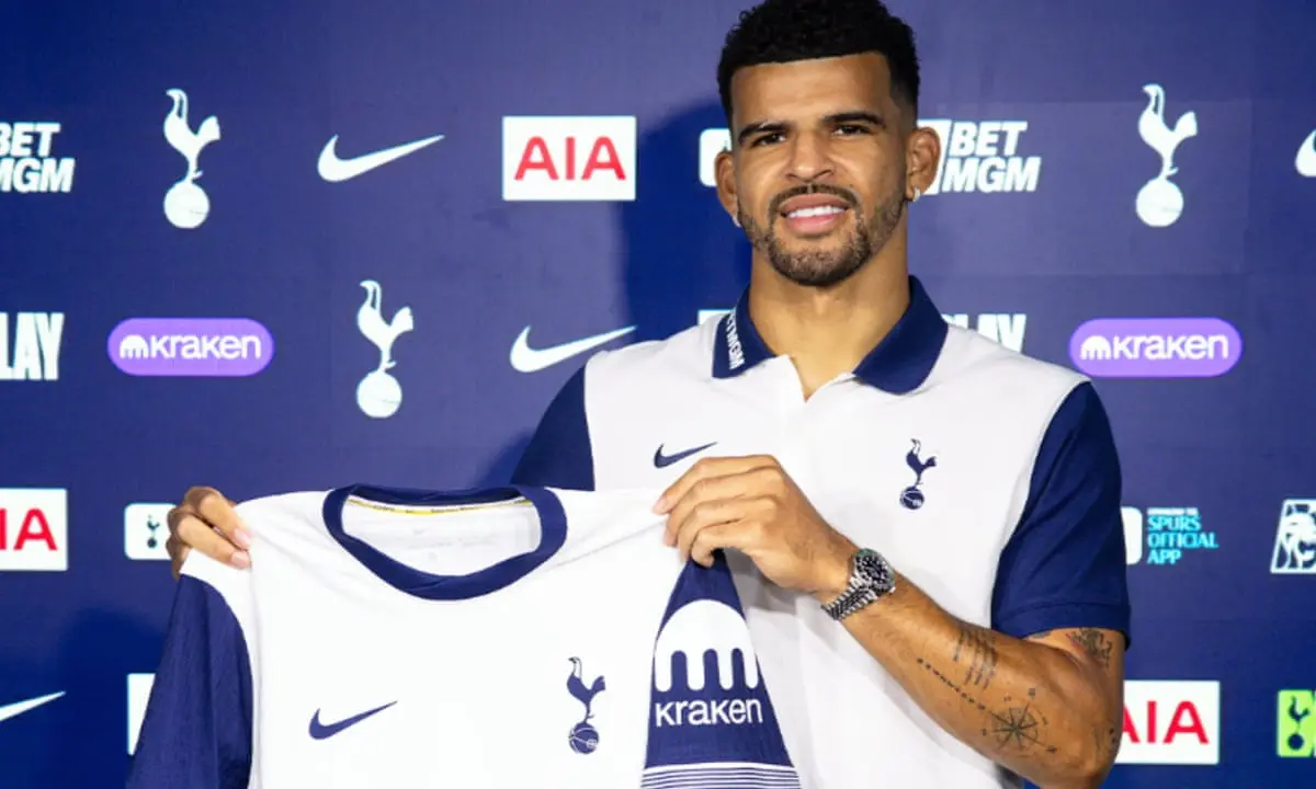 Dominic Solanke posing with a Tottenham Hotspur jersey in front of a club sponsor backdrop