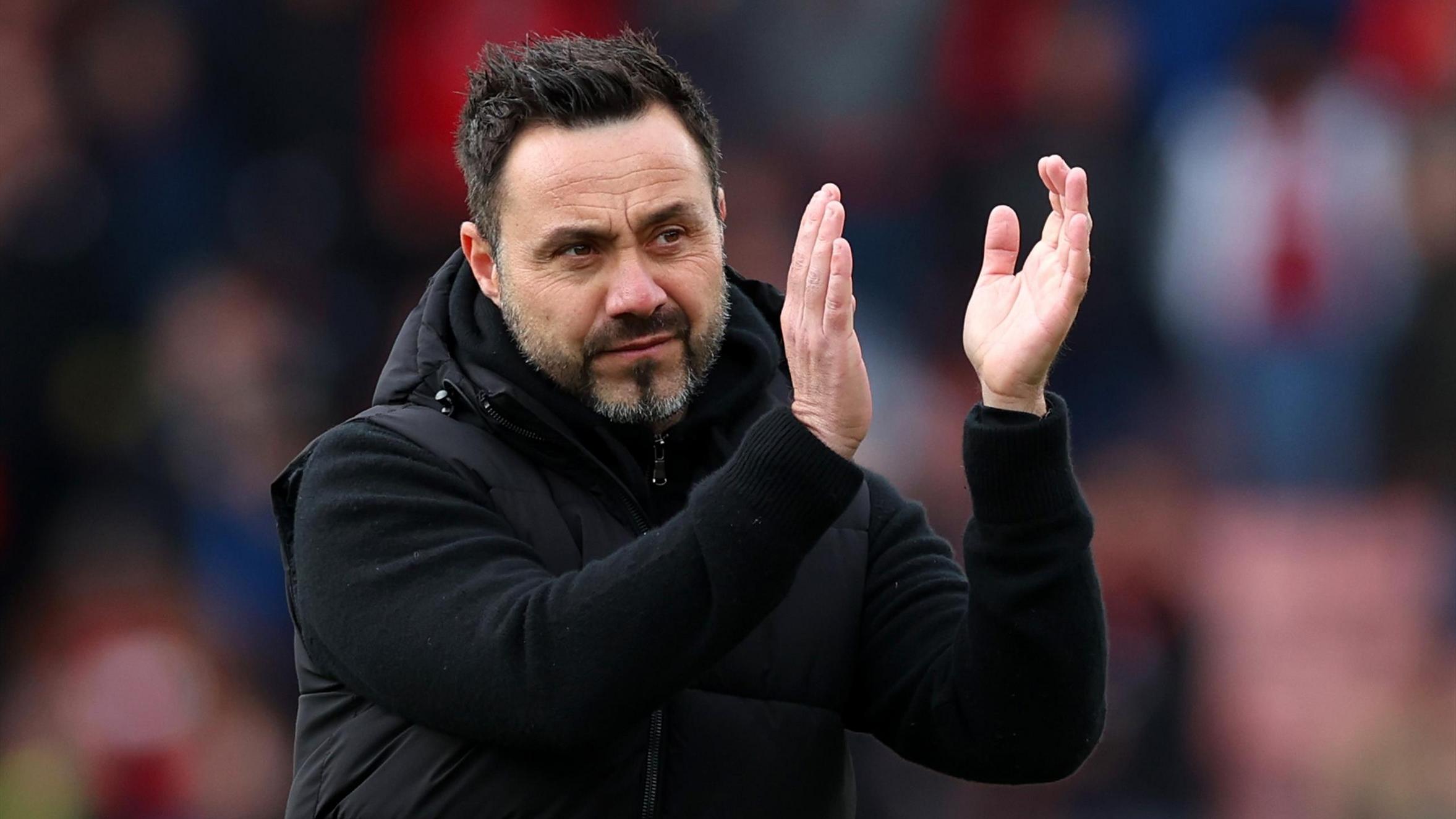 Roberto De Zerbi clapping, wearing a black jacket, during a football match.