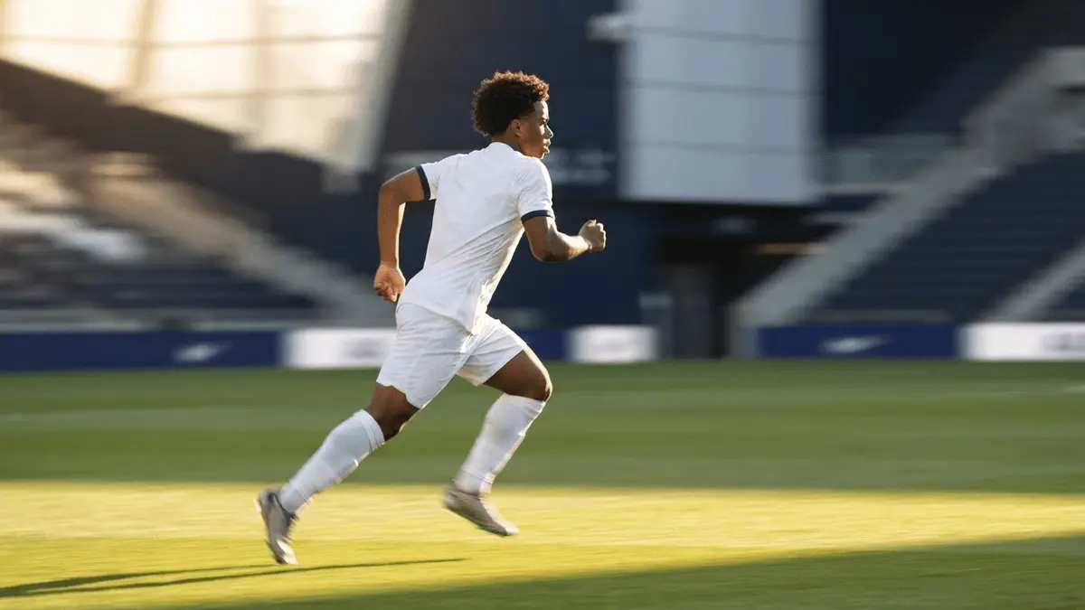 Brazilian winger sprinting down left flank in white Tottenham kit under golden hour lighting