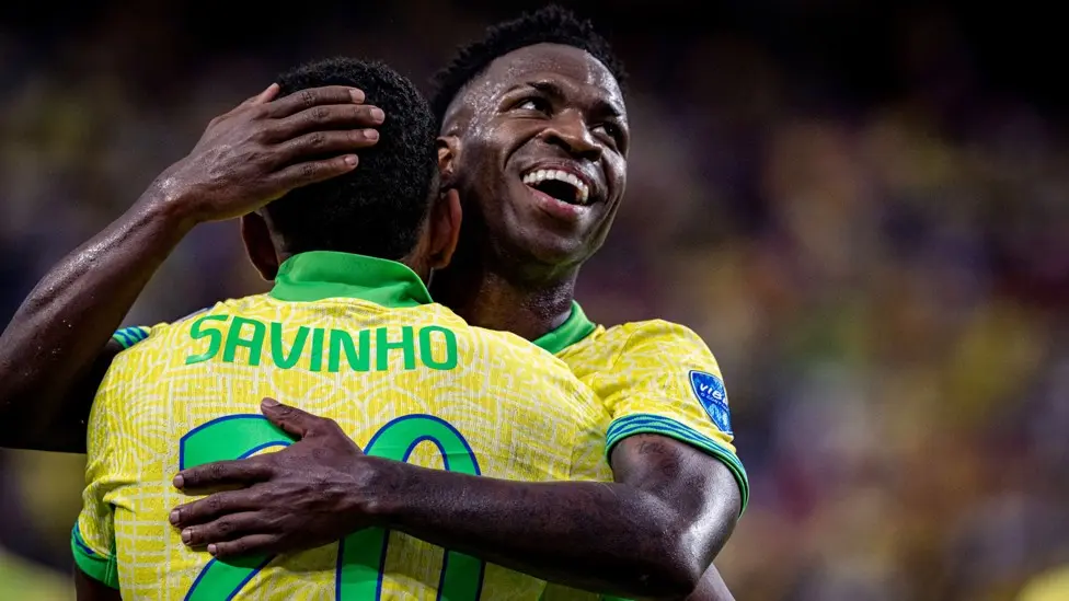Two Brazilian soccer players celebrating, one wearing a shirt with 'SAVINHO' and number 20.