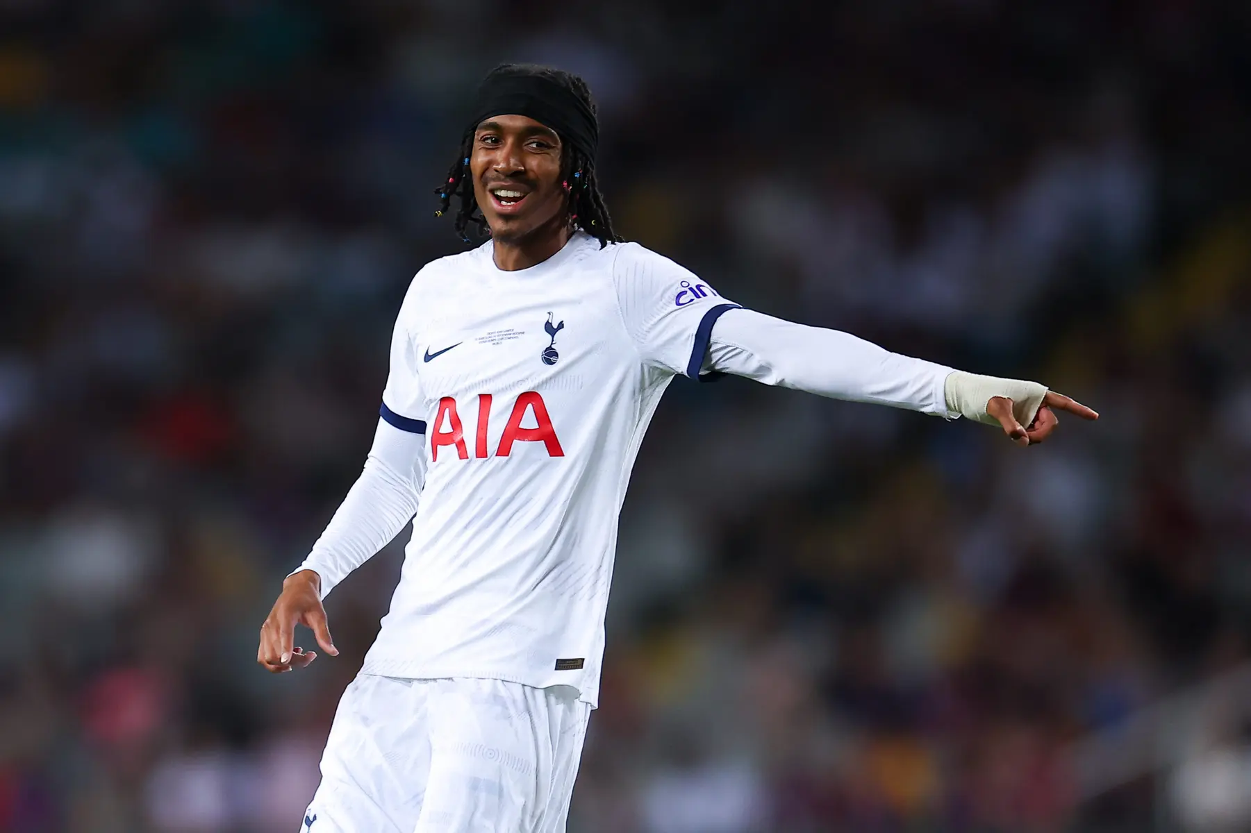 Djed Spence of Tottenham Hotspur wearing a white home kit and black headband on the pitch