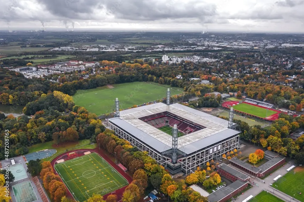 Aerial view of the RheinEnergieStadion in Cologne surrounded by autumn trees and training pitches.