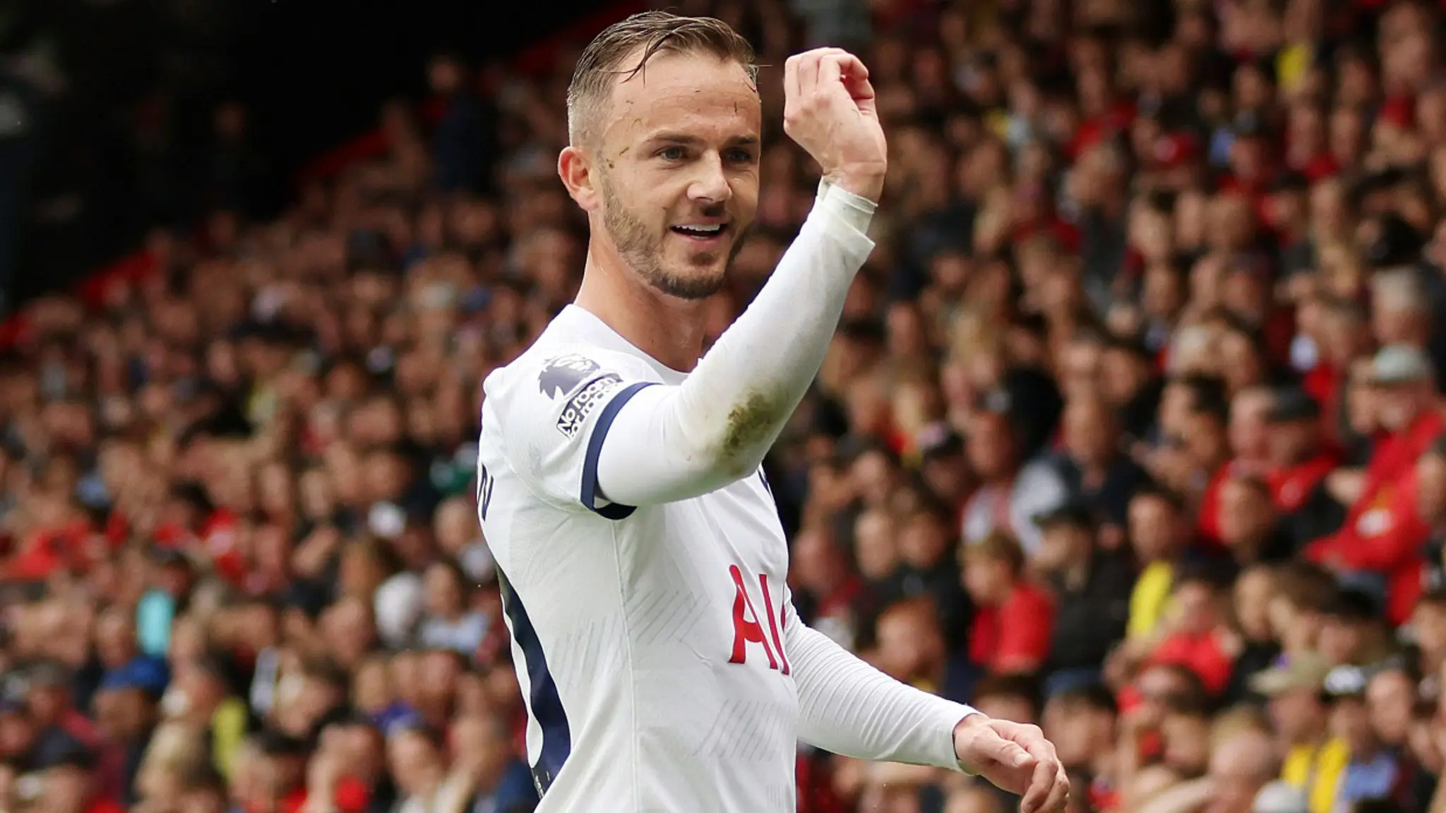 James Maddison in a white Tottenham Hotspur kit celebrating on the pitch with a crowd in the background