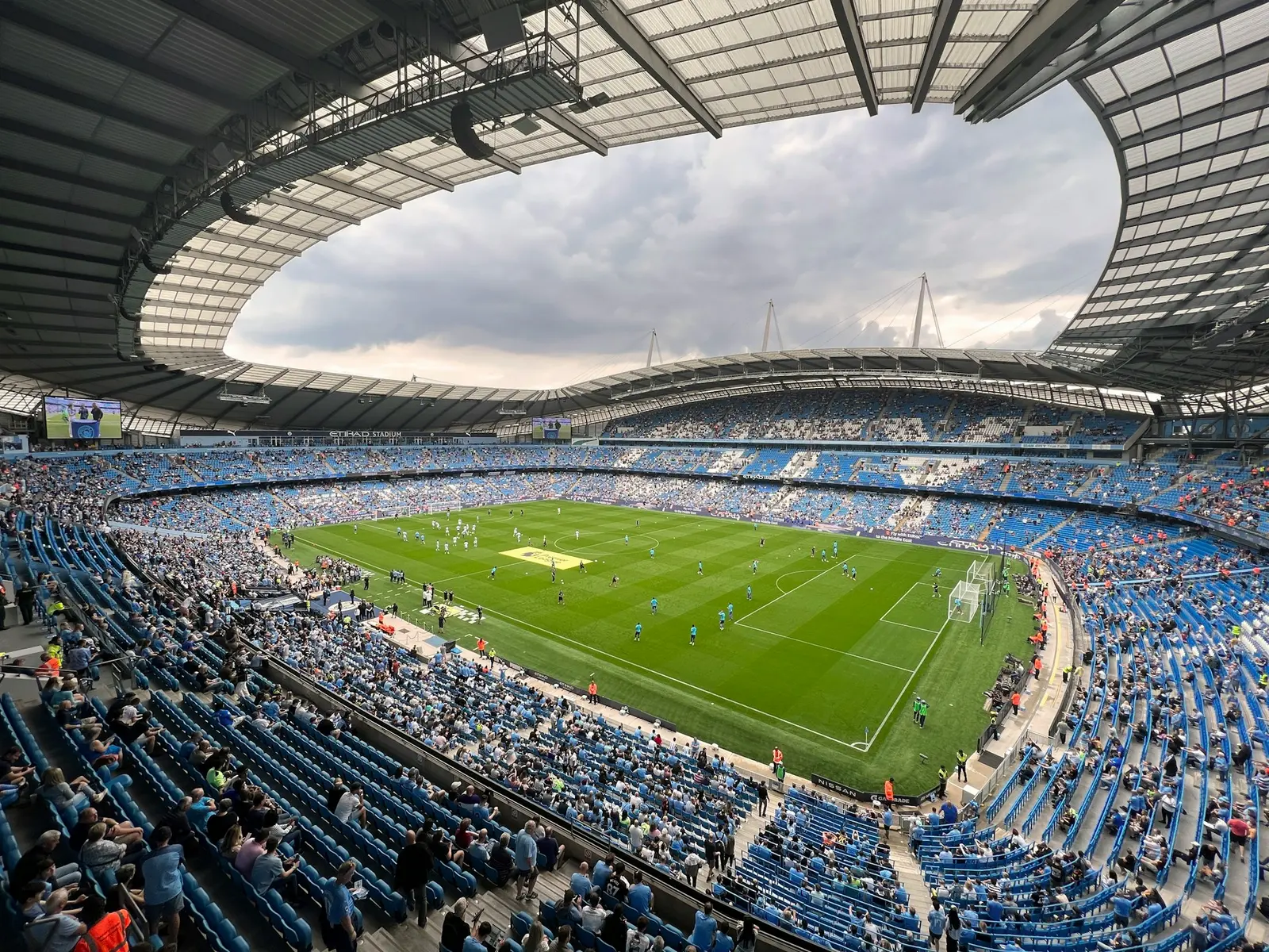 Wide view of the Etihad Stadium during a Manchester City match with fans in blue seats.