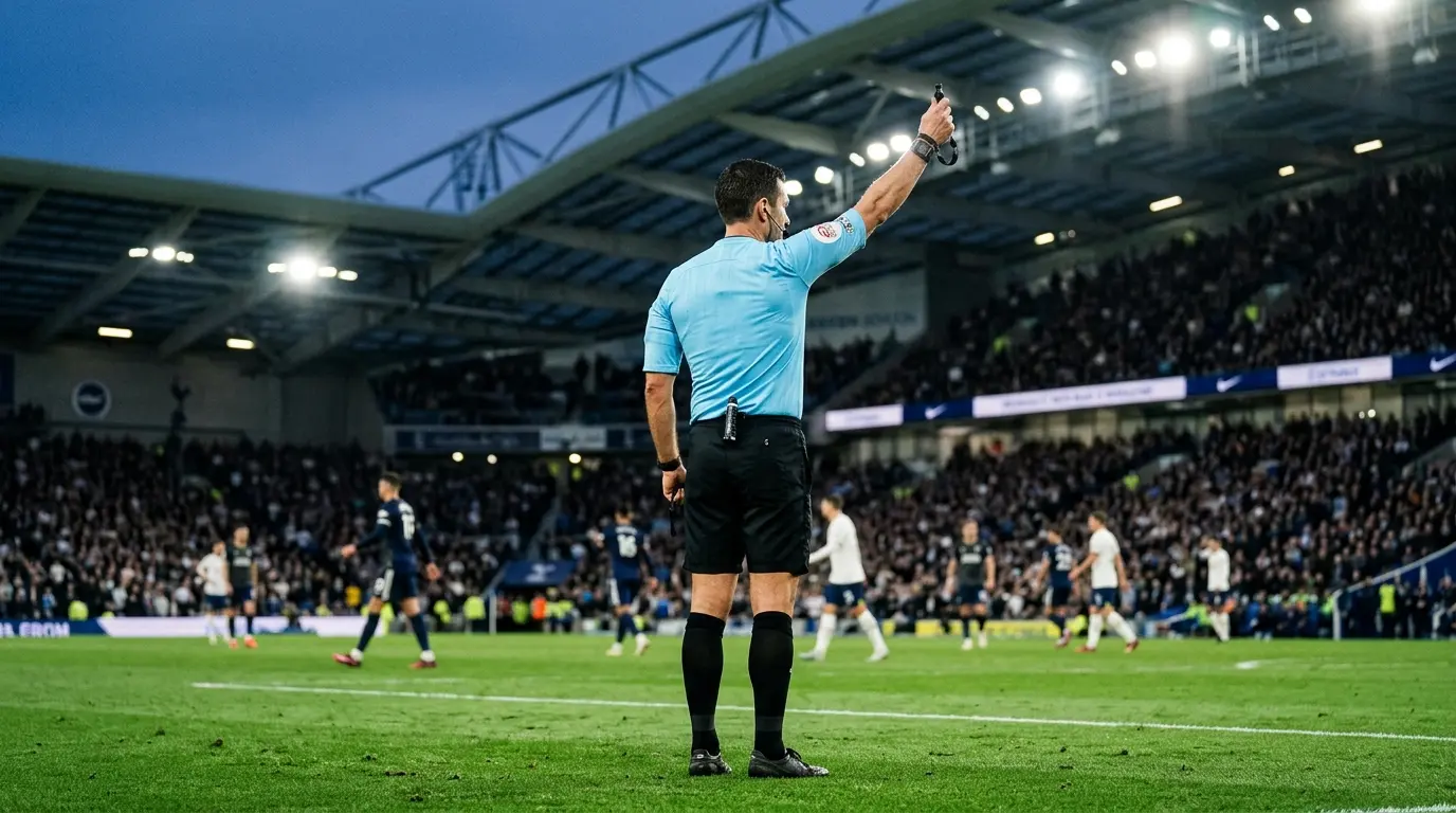 Non-identifiable football referee in a light blue kit making a decisive gesture under stadium floodlights