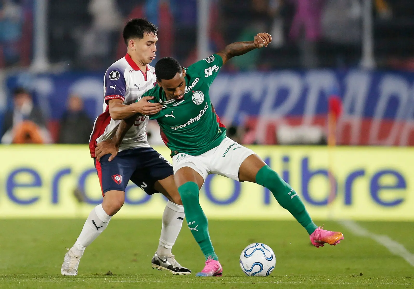 Savinho in a green Sporting Gijón kit battling for the ball against an opposing player.