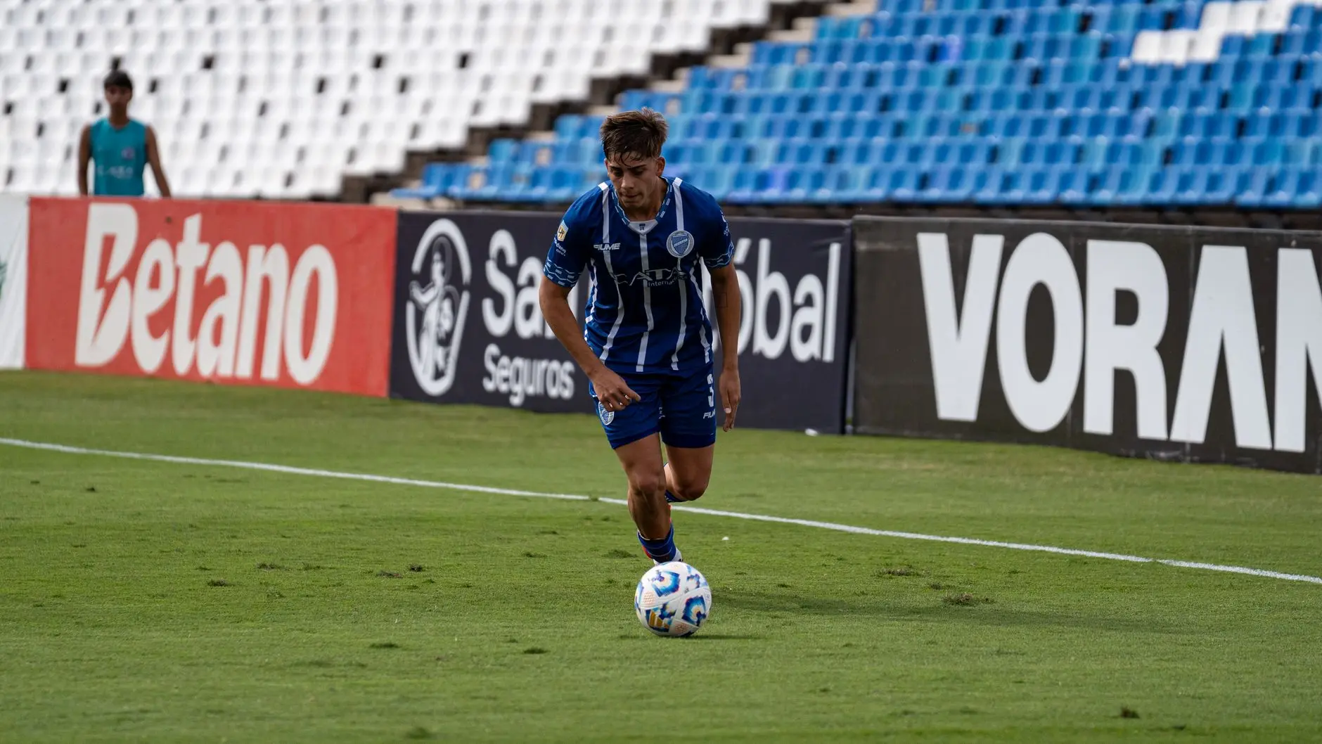 Savinho in a blue and white striped jersey dribbling a soccer ball on a grass field.