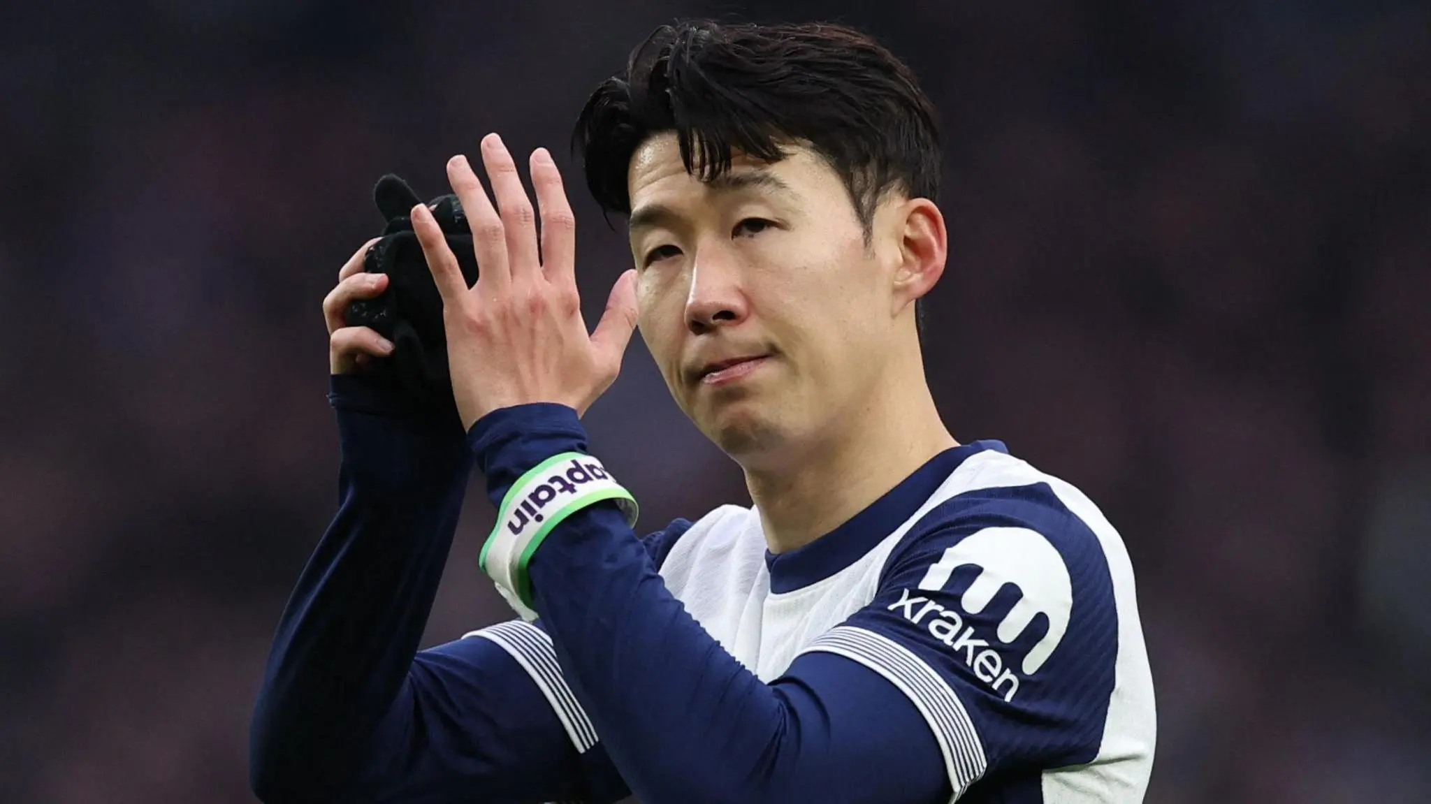 Son Heung-min in a Tottenham Hotspur kit, wearing a captain's armband and clapping.
