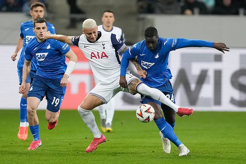 Tottenham Hotspur player in white kit challenging for the ball against two TSG Hoffenheim players in blue kits
