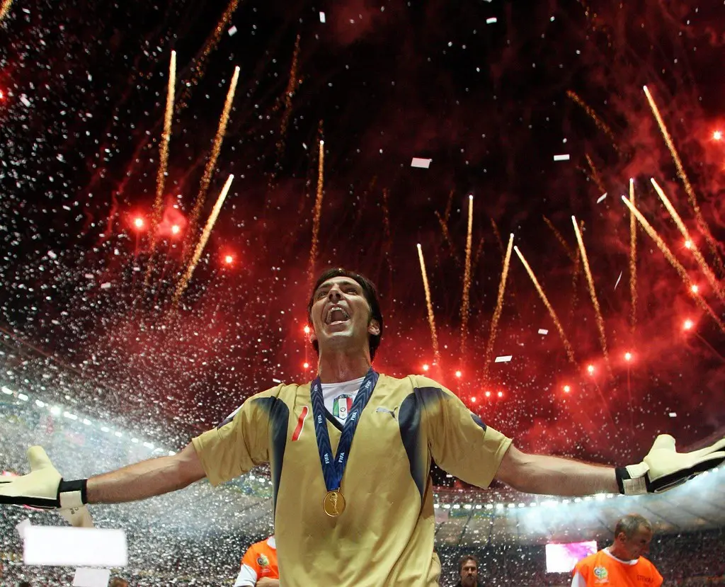 Gianluigi Buffon celebrating with a gold medal around his neck amidst confetti and fireworks.