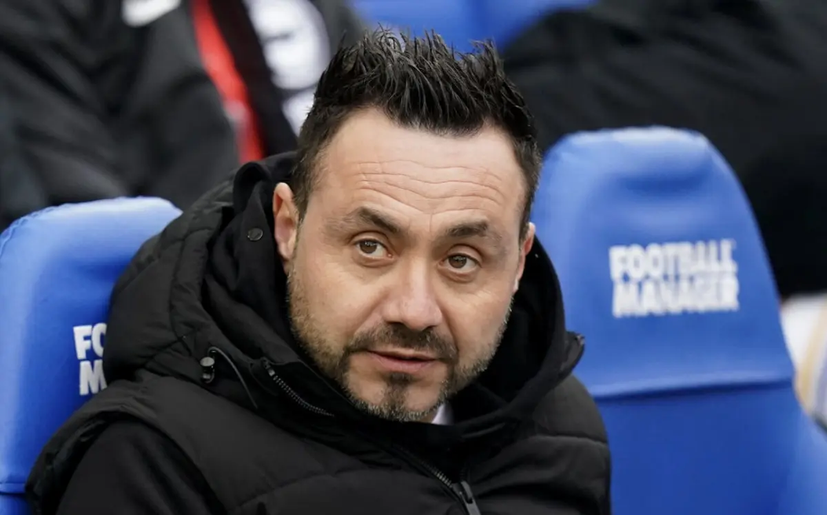 Roberto De Zerbi wearing a black jacket sitting in a blue stadium seat.