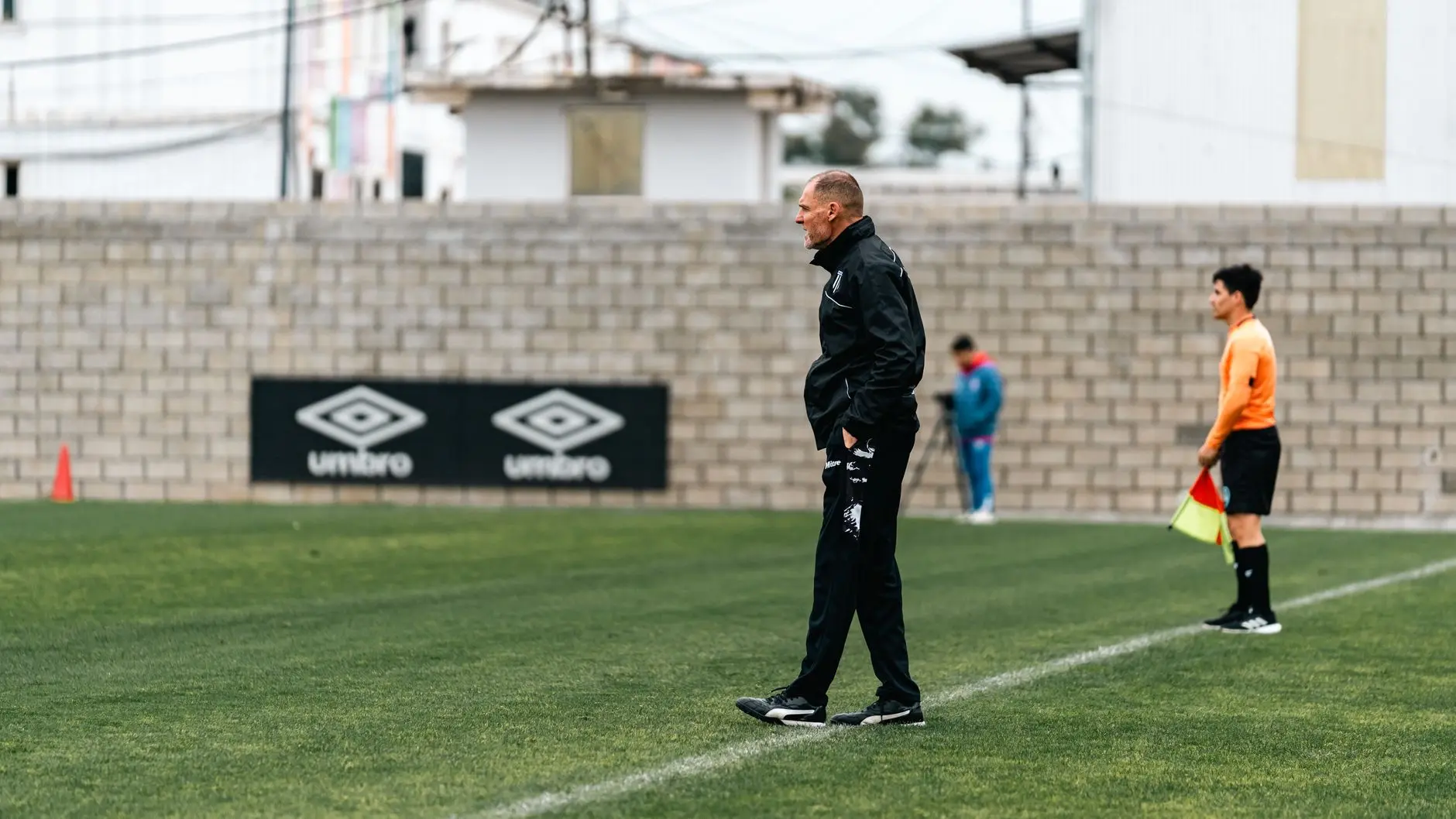 Roberto De Zerbi walking on the sidelines of a football pitch wearing a black tracksuit