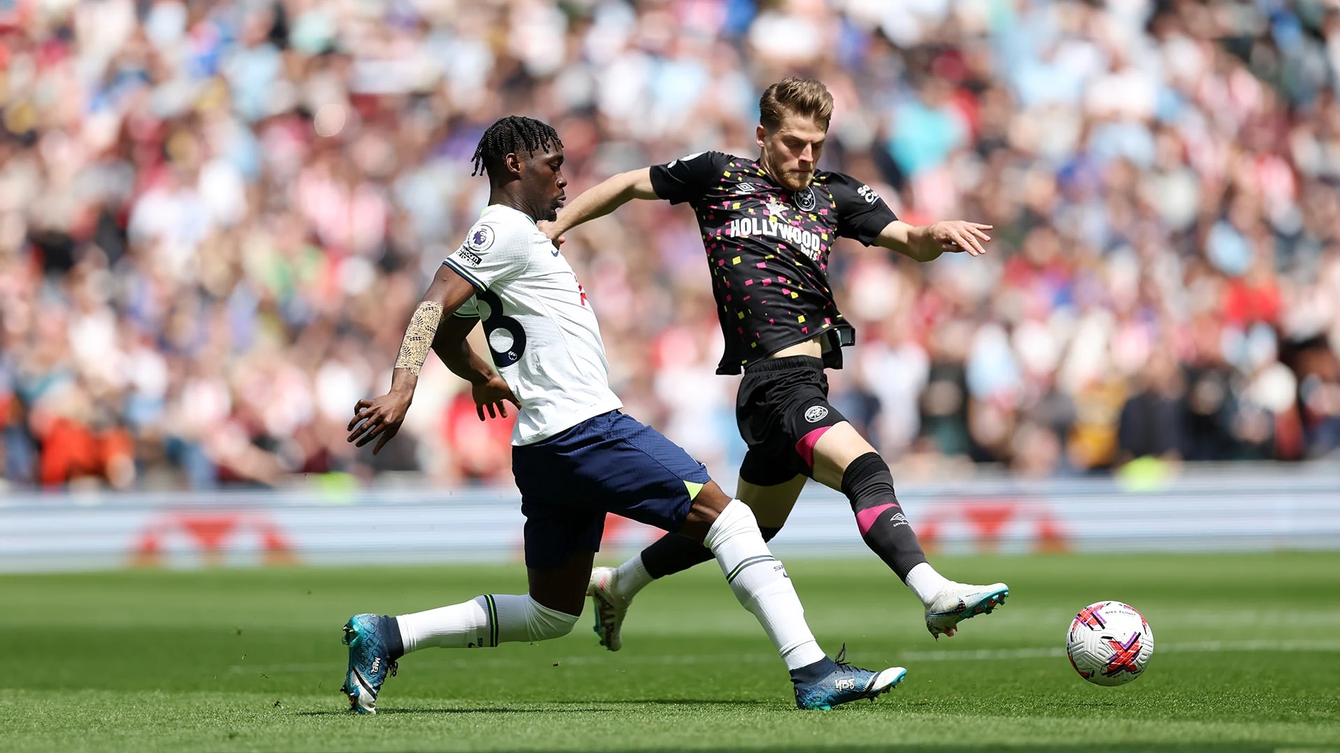 A Tottenham Hotspur player in a white kit competes for the ball against a Brentford player in a black kit.
