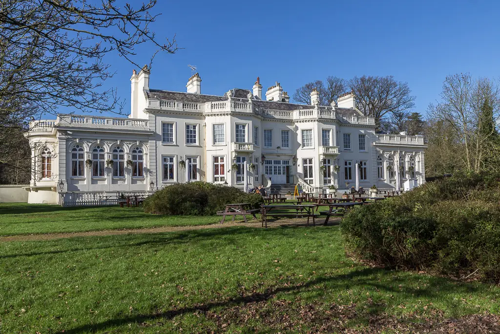 A large, white historic mansion with classical architecture and a grassy lawn in front.